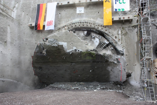 Zu sehen ist der Moment des Durchbruchs eines Tunnelvortriebs. An der Geländeoberfläche hängen u.a. die deutsche Flagge und die der DB.